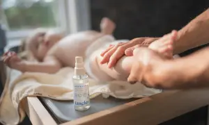 En bebis får massage med babyolja i håret och på kroppen. En flaska med Tangles babyolja står bredvid.