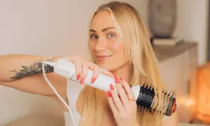 Blond kvinna med tatuering på armen använder en stylingborste för att skapa volym och glans i sitt blow out hår.
