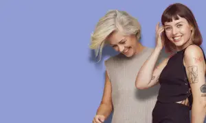 Två kvinnor ler mot kameran. Den ena har en kort rufsig frisyr och grått hår, den andra har mörkt hår och tatueringar.