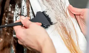 Hårstylist applicerar blekning på mörkt hår för att skapa ljusare slingor.