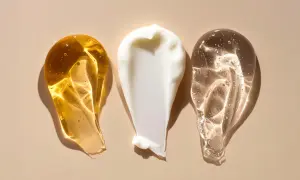 Tre olika krämsprut på en beige bakgrund. En gyllene, en vit och en genomskinlig. Kanske en blandning av retinol och c-vitamin för huden.