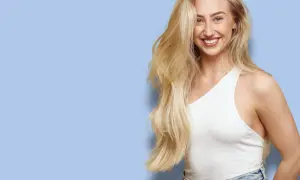Glad kvinna med långt, blonderat hår som skrattar. Hon bär en vit topp och jeans.