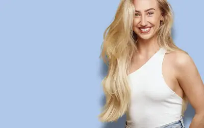 Glad kvinna med långt, blonderat hår som skrattar. Hon bär en vit topp och jeans.