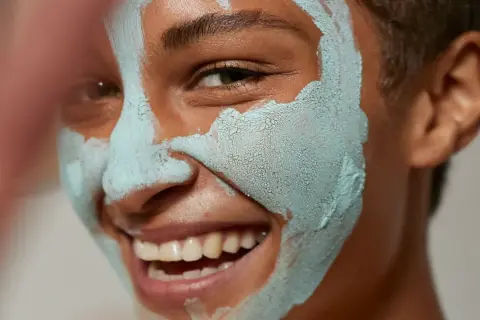 Glad person med lermask som rengör porer.