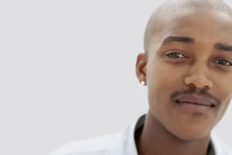 En ung man med rakad skalle och en diskret mustasch som han verkar vara nöjd med att trimma.