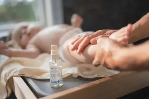 En bebis får massage med babyolja i håret och på kroppen. En flaska med Tangles babyolja står bredvid.