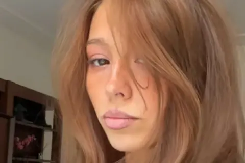En ung kvinna med hår som skiftar från blond till brunett, med en mjuk blick.