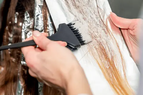 Hårstylist applicerar blekning på mörkt hår för att skapa ljusare slingor.