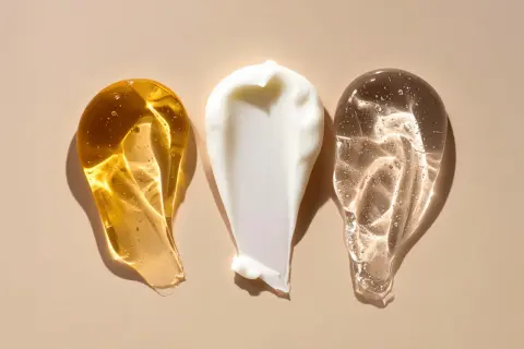 Tre olika krämsprut på en beige bakgrund. En gyllene, en vit och en genomskinlig. Kanske en blandning av retinol och c-vitamin för huden.