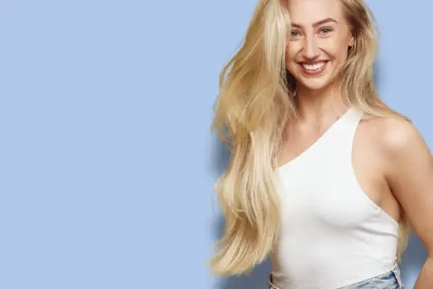 Glad kvinna med långt, blonderat hår som skrattar. Hon bär en vit topp och jeans.