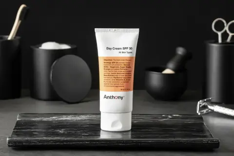 En tub med dagkräm SPF 30 från Anthony står i fokus. Runtomkring syns accessoarer som en rakhyvel och borste, vilket antyder en komplett hudvårdsrutin ordning.