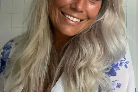 Glad kvinna med blont, vågigt hår som vill få rakt hår utan plattång. Hon ler och har en blåvit blommig klänning.