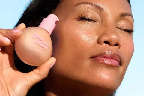 En hand håller en flaska "Glow and Plump" hudserum. Ansiktet visar en naturlig glow up med glansiga läppar.