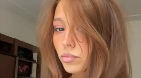 En ung kvinna med hår som skiftar från blond till brunett, med en mjuk blick.