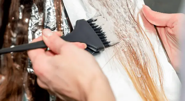 Hårstylist applicerar blekning på mörkt hår för att skapa ljusare slingor.