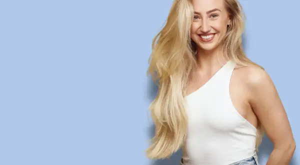 Glad kvinna med långt, blonderat hår som skrattar. Hon bär en vit topp och jeans.