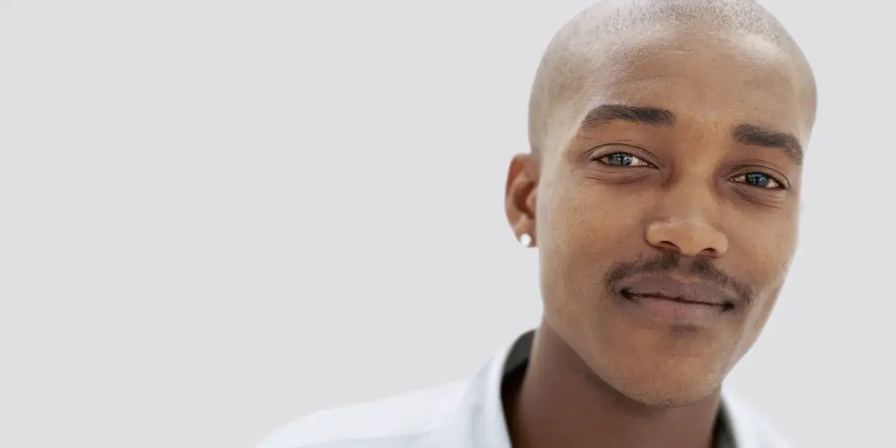 En ung man med rakad skalle och en diskret mustasch som han verkar vara nöjd med att trimma.