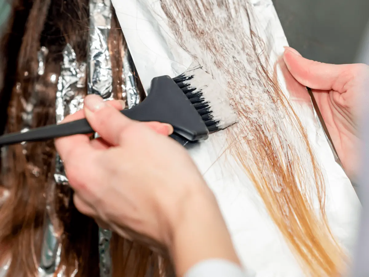 Hårstylist applicerar blekning på mörkt hår för att skapa ljusare slingor.