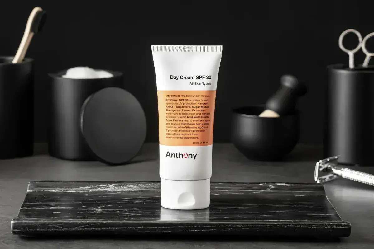En tub med dagkräm SPF 30 från Anthony står i fokus. Runtomkring syns accessoarer som en rakhyvel och borste, vilket antyder en komplett hudvårdsrutin ordning.