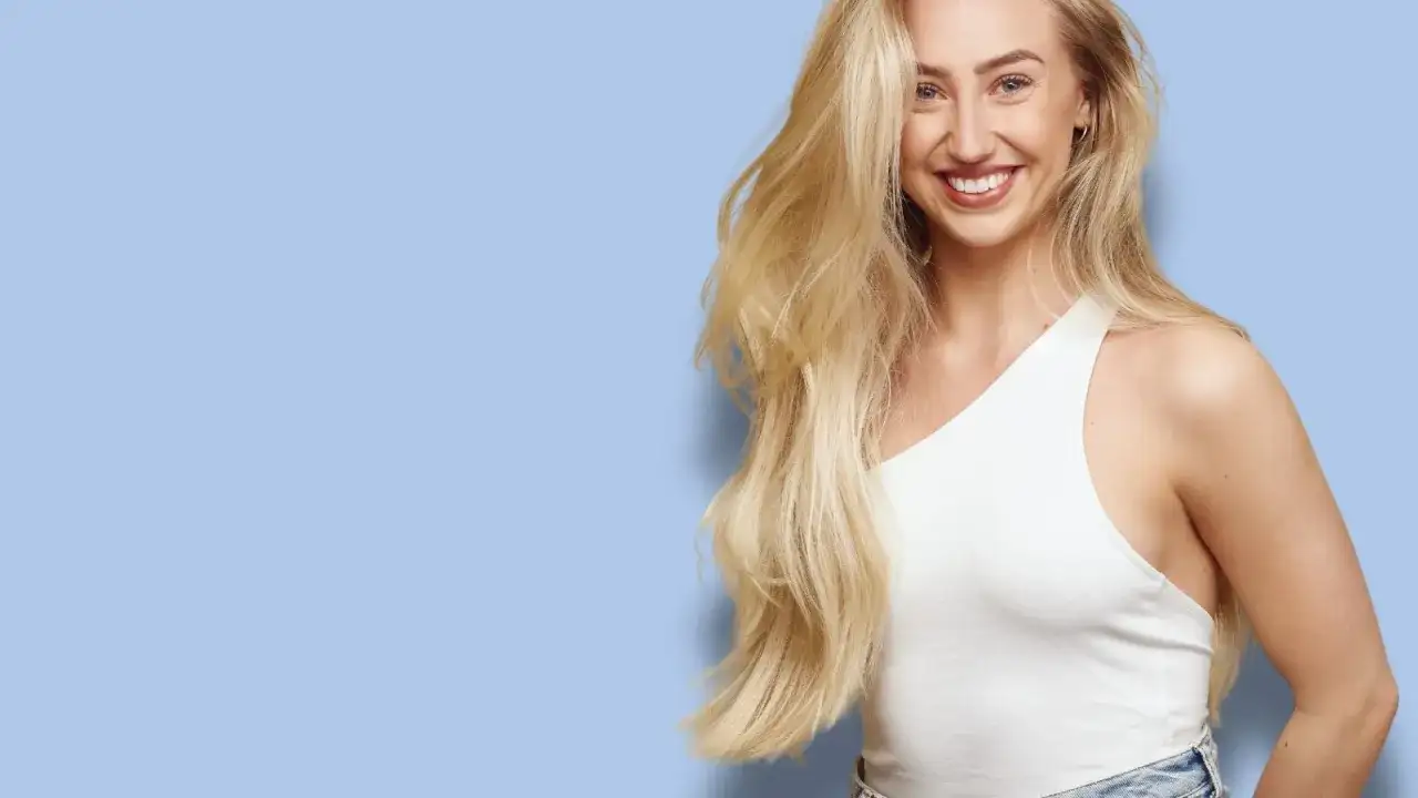 Glad kvinna med långt, blonderat hår som skrattar. Hon bär en vit topp och jeans.