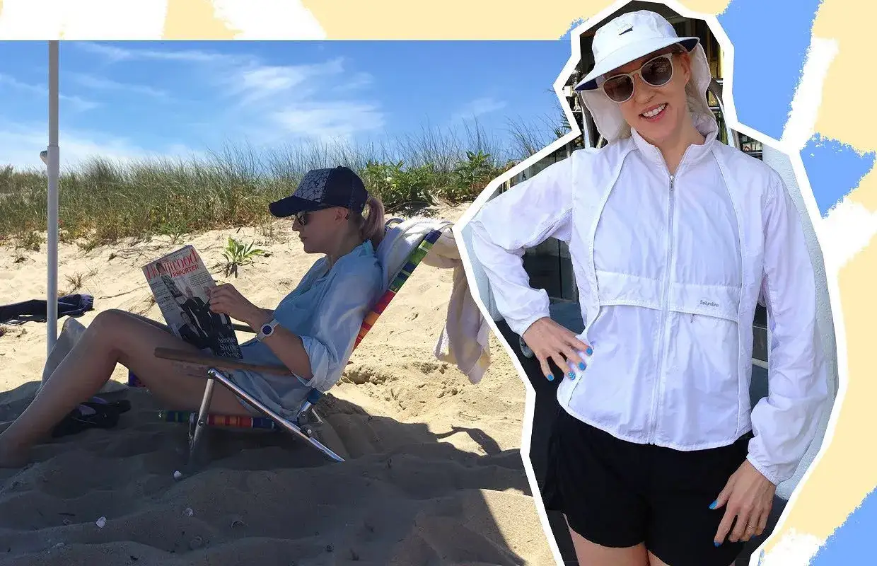 Kvinna på stranden läser tidning, skyddar sitt hud organ med solhatt och jacka.