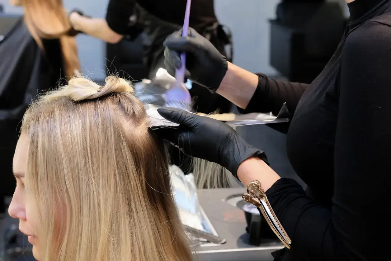 Fris&ouml;r applicerar f&auml;rg i en kunds ljusblonda h&aring;r.
