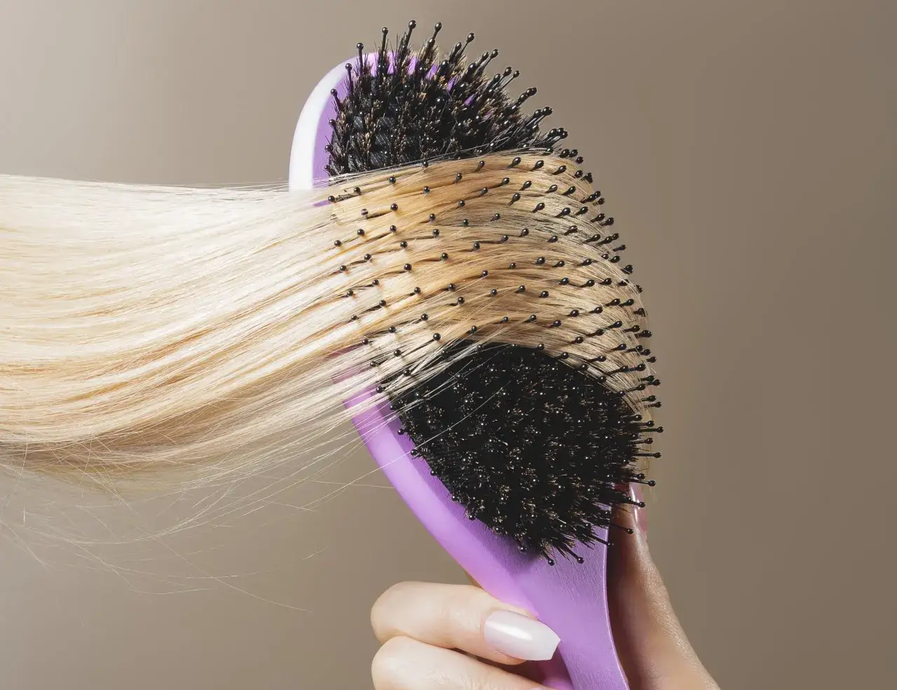 En hand h&aring;ller en lila borste som borstar blont h&aring;r. H&aring;ret ser lite torrt ut, kanske med torra toppar.