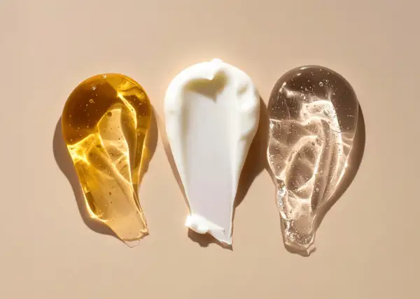 Tre olika krämsprut på en beige bakgrund. En gyllene, en vit och en genomskinlig. Kanske en blandning av retinol och c-vitamin för huden.