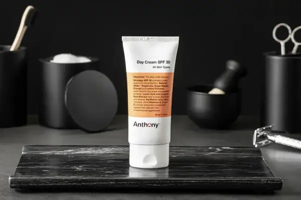 En tub med dagkräm SPF 30 från Anthony står i fokus. Runtomkring syns accessoarer som en rakhyvel och borste, vilket antyder en komplett hudvårdsrutin ordning.