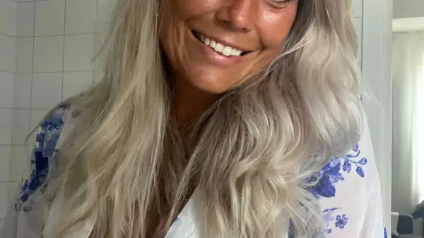 Glad kvinna med blont, vågigt hår som vill få rakt hår utan plattång. Hon ler och har en blåvit blommig klänning.