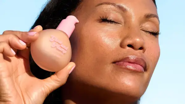 En hand håller en flaska "Glow and Plump" hudserum. Ansiktet visar en naturlig glow up med glansiga läppar.